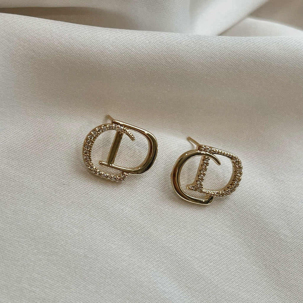 Gold crystal stud earrings with pavé detailing styled on soft ivory satin fabric