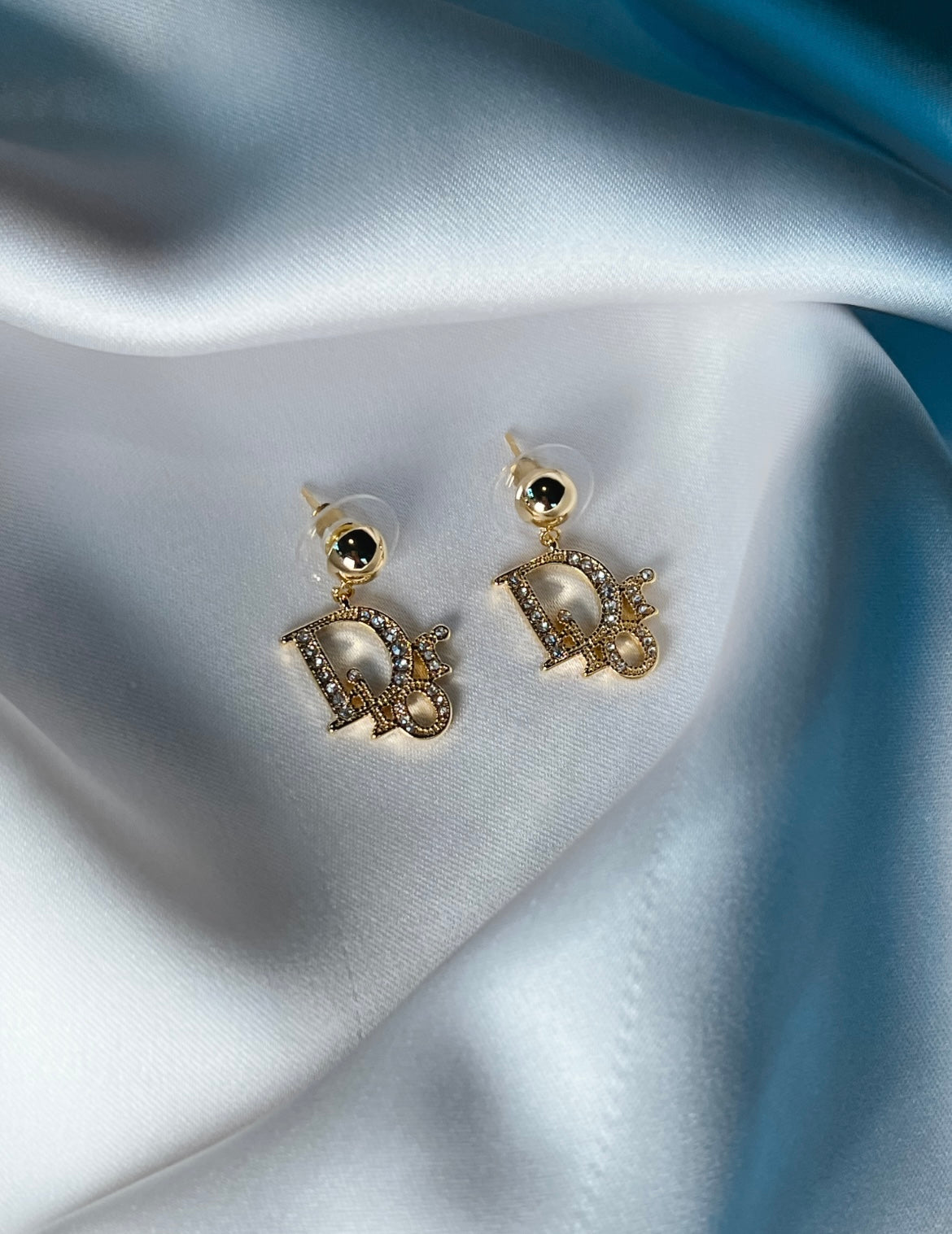 Gold statement drop earrings with crystal embellishments styled on soft ivory satin fabric